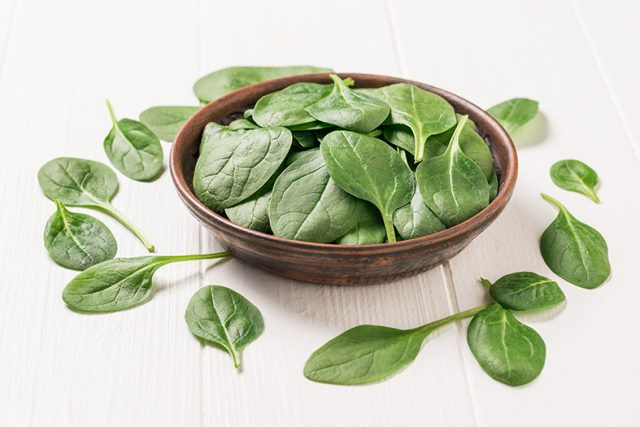A large number of spinach leaves on a white wooden table. Food for fitness. The view from the top.
