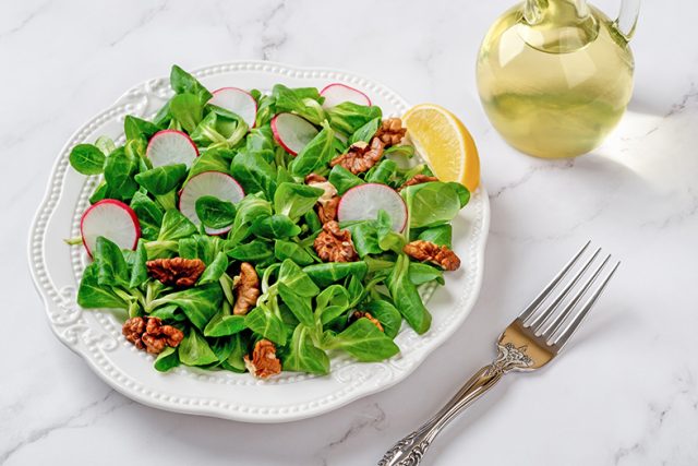 Lambs lettuce salad with radish and walnuts. Cornsalad leaves, nut kernels and sliced radish on a white plate against marble surface. Low calories slimming diet with vitamin vegetable salad.